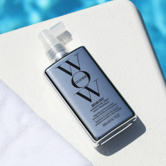 Color Wow Produkt auf einer hellen Oberfläche neben einem Handtuch und blauem Wasser im Hintergrund.