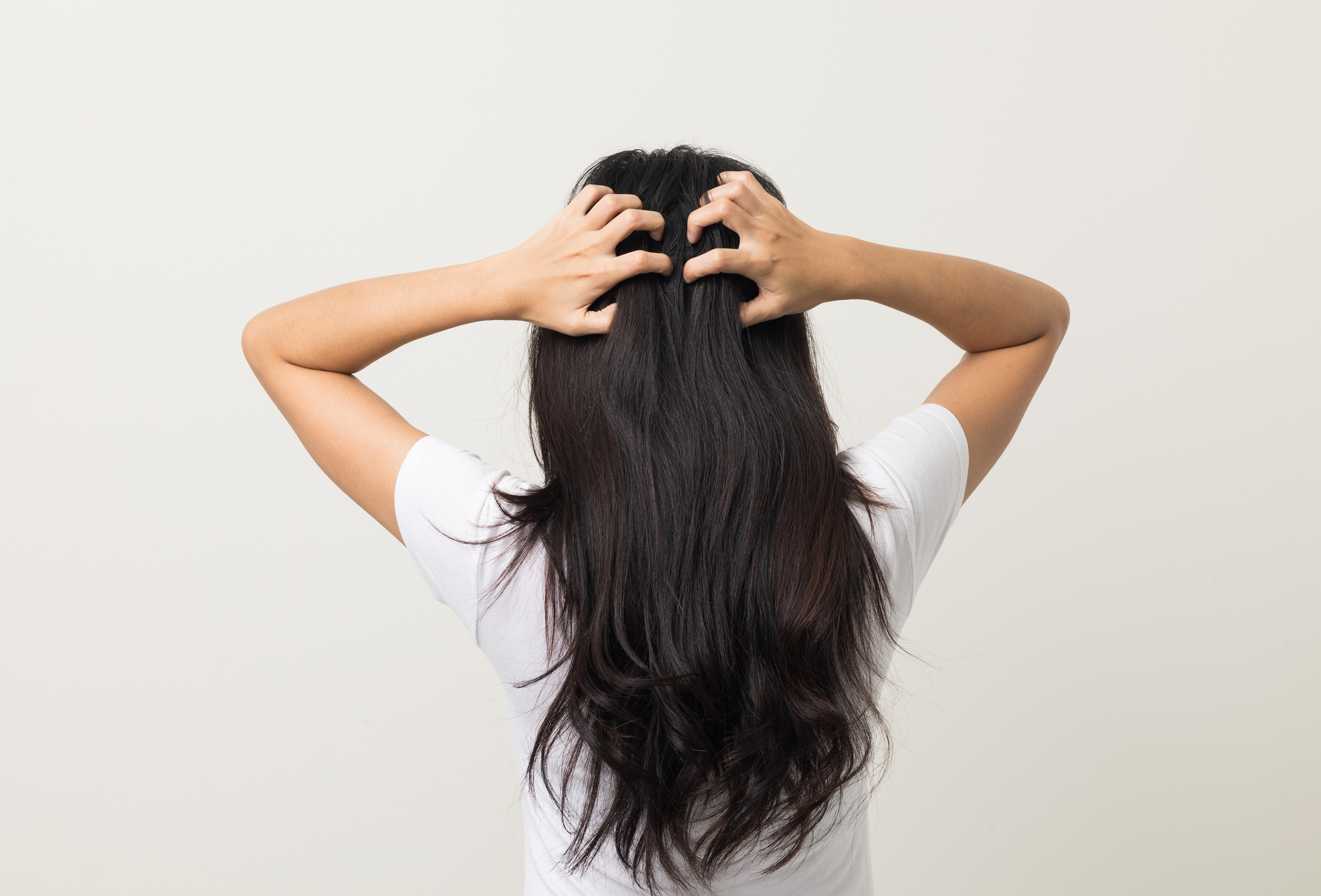 Frau mit langen dunklen Haaren greift sich auf die Kopfhaut
