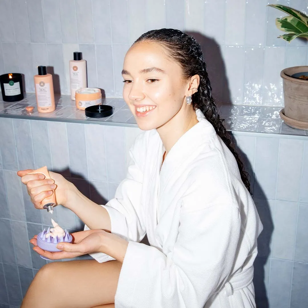 Frau im Bademantel mit Maria Nila Scalp Brush in der Hand